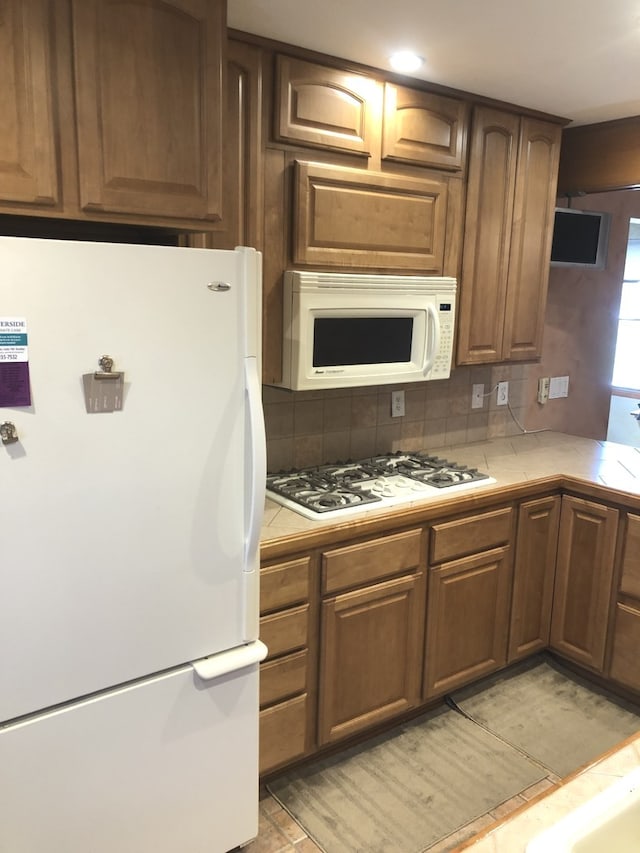 kitchen featuring tile countertops, tasteful backsplash, and white appliances