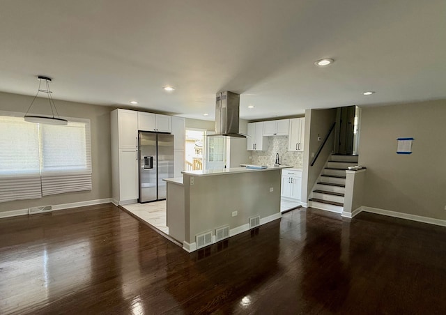 kitchen with white cabinets, pendant lighting, wall chimney exhaust hood, stainless steel refrigerator with ice dispenser, and hardwood / wood-style floors