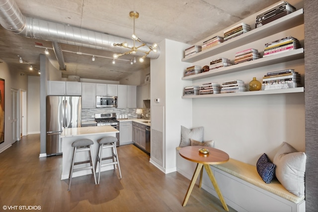 kitchen with decorative light fixtures, backsplash, dark wood-type flooring, stainless steel appliances, and a kitchen breakfast bar