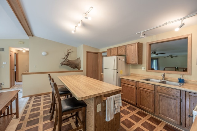 kitchen with lofted ceiling with beams, white refrigerator, a kitchen bar, a center island, and sink