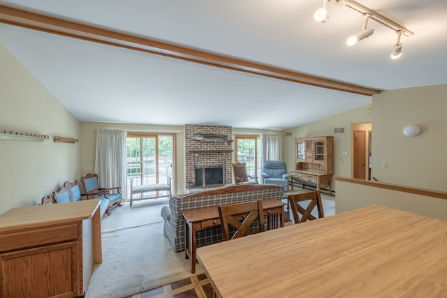 dining space with vaulted ceiling with beams, a brick fireplace, track lighting, light carpet, and a baseboard radiator