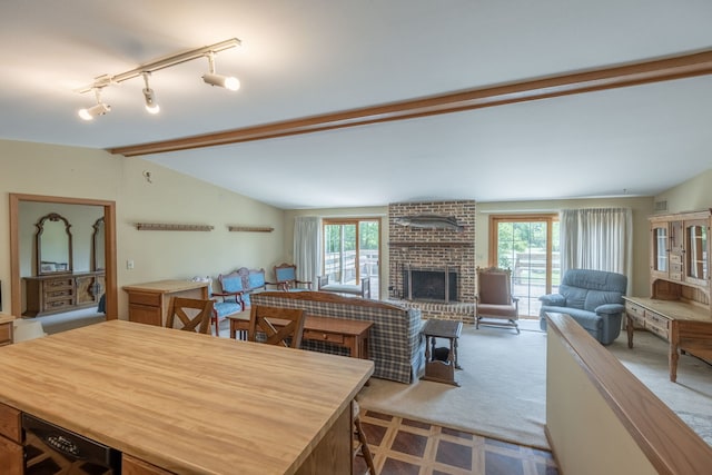 carpeted dining room featuring rail lighting, a healthy amount of sunlight, vaulted ceiling, and a brick fireplace