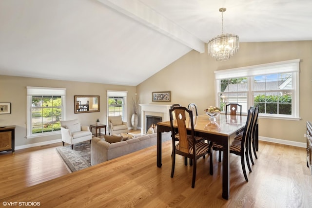 dining space with baseboards, a chandelier, lofted ceiling with beams, light wood-style flooring, and a warm lit fireplace