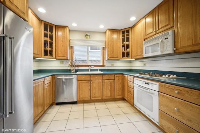 kitchen with dark countertops, light tile patterned floors, appliances with stainless steel finishes, brown cabinetry, and a sink