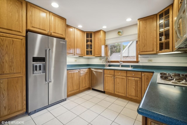 kitchen with brown cabinets, a sink, dark countertops, stainless steel appliances, and light tile patterned flooring