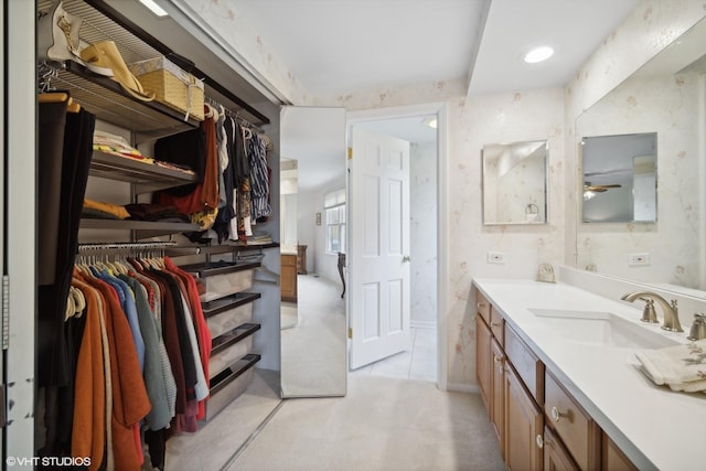 bathroom with vanity, a walk in closet, a ceiling fan, and wallpapered walls