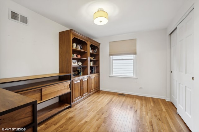 home office with light wood finished floors, visible vents, and baseboards