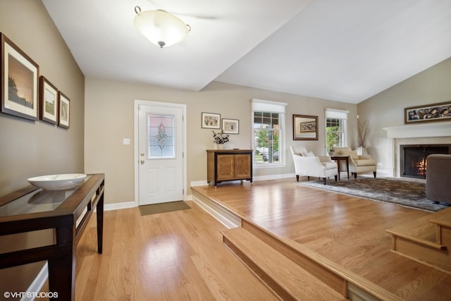 foyer with baseboards, lofted ceiling, a warm lit fireplace, and light wood finished floors