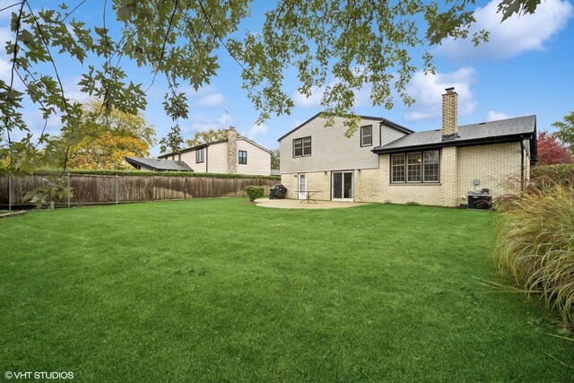 rear view of house featuring fence, a chimney, a lawn, a patio area, and brick siding