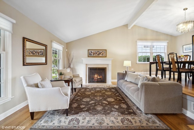 living area featuring a lit fireplace, a healthy amount of sunlight, wood finished floors, and vaulted ceiling with beams