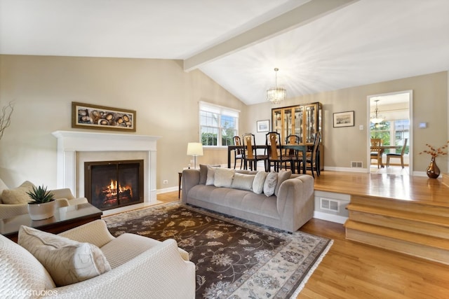 living room with visible vents, vaulted ceiling with beams, a fireplace with flush hearth, an inviting chandelier, and wood finished floors