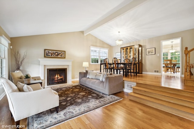 living room featuring wood finished floors, visible vents, vaulted ceiling with beams, a lit fireplace, and a notable chandelier