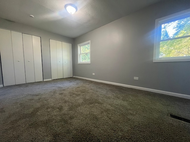 unfurnished bedroom featuring a textured ceiling, two closets, and carpet