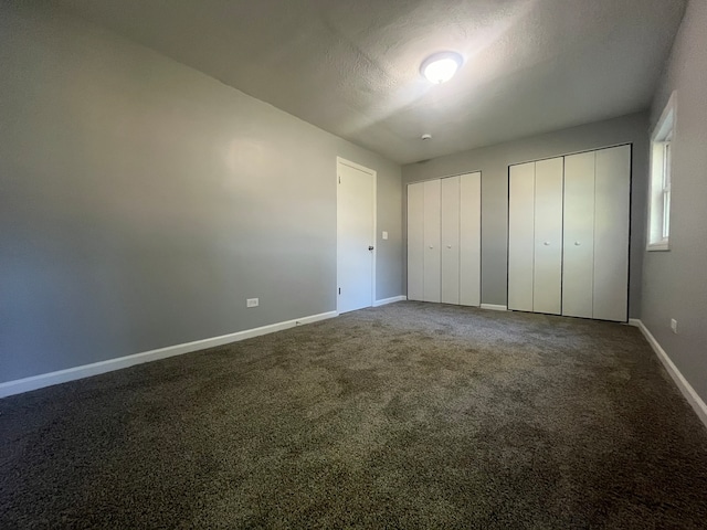 unfurnished bedroom featuring carpet flooring, a textured ceiling, and two closets