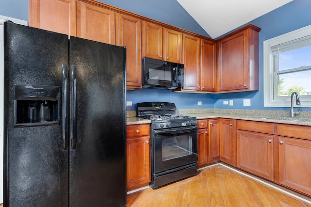 kitchen with light hardwood / wood-style flooring, sink, light stone countertops, black appliances, and vaulted ceiling