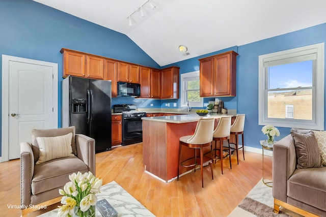 kitchen with a kitchen bar, vaulted ceiling, black appliances, light hardwood / wood-style floors, and sink