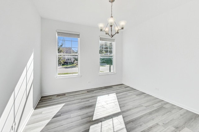 spare room with a notable chandelier and light wood-type flooring