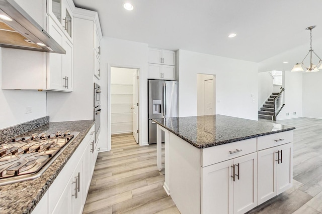 kitchen featuring light wood-type flooring, stainless steel appliances, decorative light fixtures, white cabinets, and extractor fan