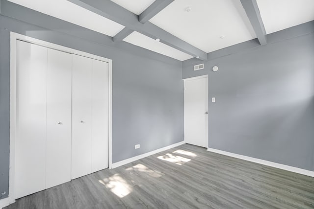 unfurnished bedroom with a closet, beam ceiling, and dark hardwood / wood-style flooring