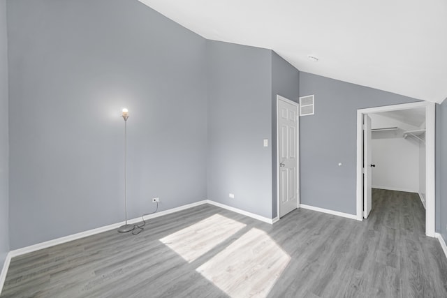 unfurnished bedroom with a closet, light wood-type flooring, vaulted ceiling, and a walk in closet