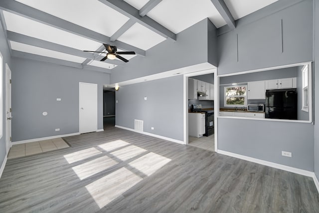 unfurnished living room featuring ceiling fan, beamed ceiling, and light hardwood / wood-style flooring