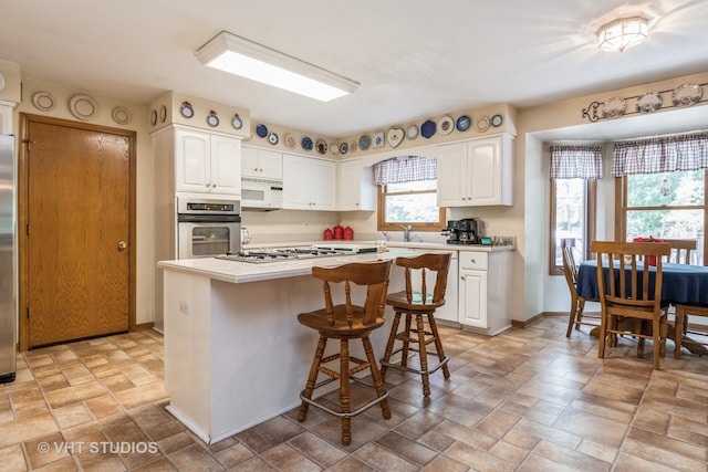 kitchen with white cabinets, sink, stainless steel appliances, a kitchen breakfast bar, and a center island