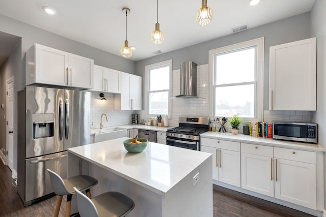 kitchen with stainless steel appliances, white cabinets, hanging light fixtures, and wall chimney exhaust hood