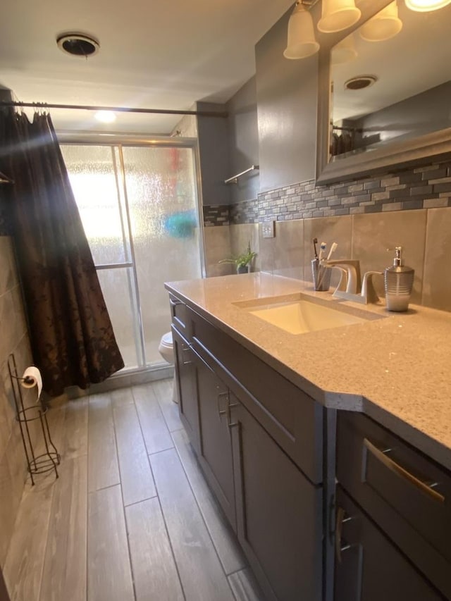 bathroom featuring curtained shower, wood-type flooring, toilet, decorative backsplash, and vanity