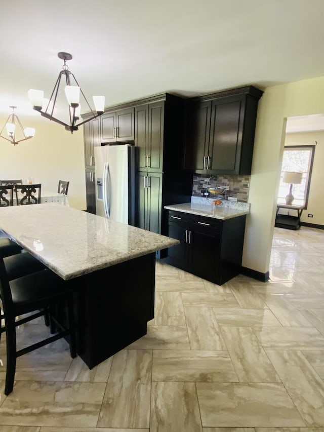 kitchen with light stone countertops, backsplash, decorative light fixtures, an inviting chandelier, and stainless steel fridge with ice dispenser