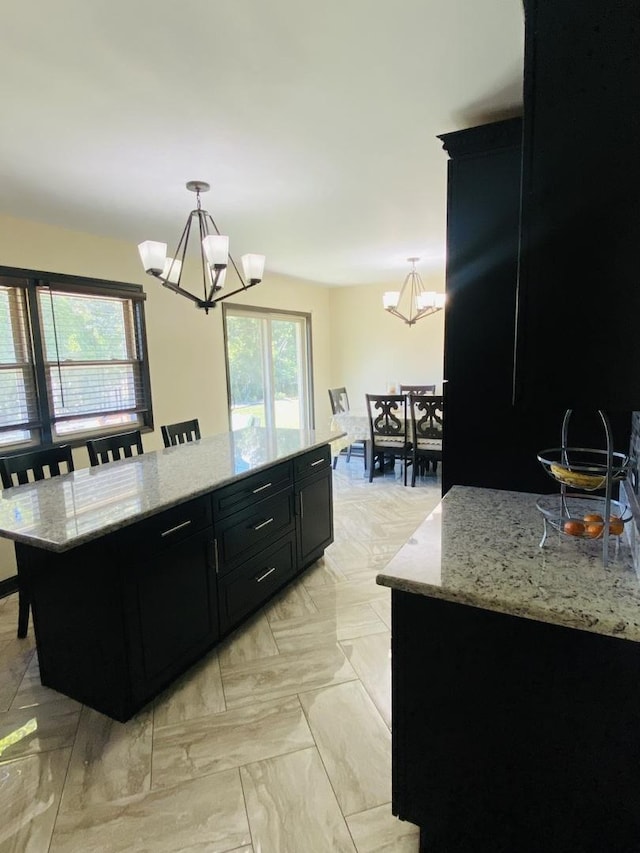 kitchen with light stone countertops, a kitchen island, decorative light fixtures, and a notable chandelier