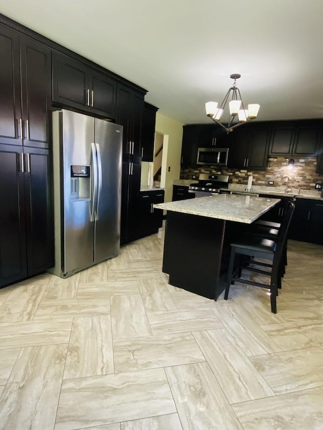 kitchen with appliances with stainless steel finishes, light stone counters, pendant lighting, a chandelier, and a kitchen island