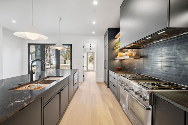 kitchen with pendant lighting, light hardwood / wood-style floors, stainless steel stove, decorative backsplash, and wall chimney exhaust hood