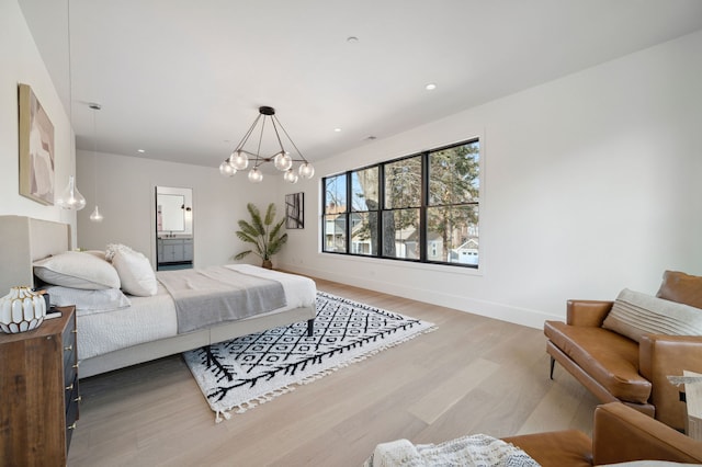 bedroom with a notable chandelier, wood-type flooring, and connected bathroom