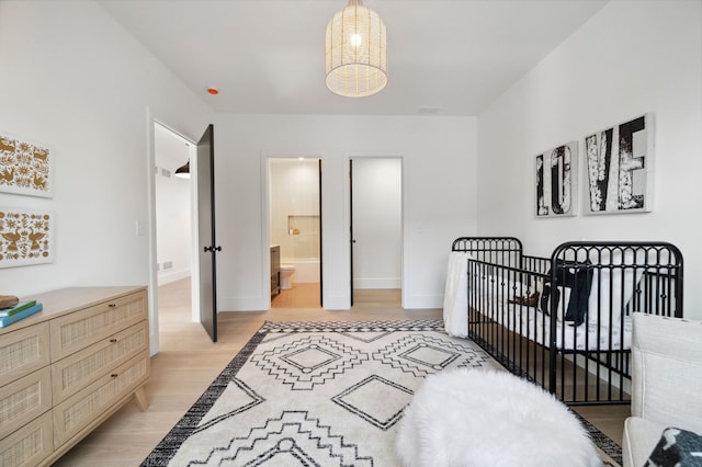 bedroom featuring a crib, connected bathroom, and light hardwood / wood-style flooring