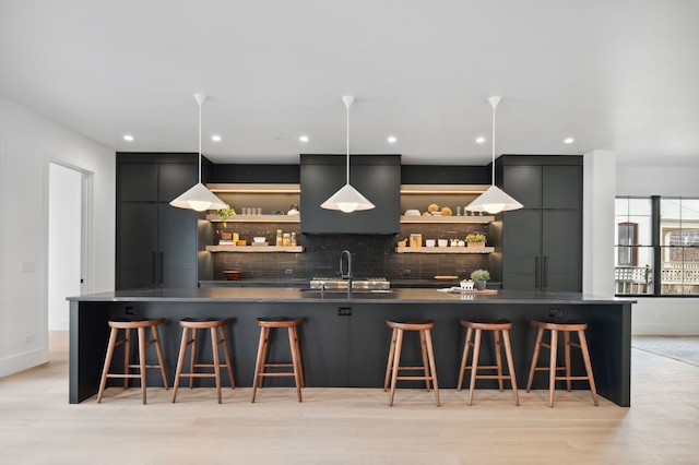 kitchen featuring light wood-type flooring, a breakfast bar area, decorative light fixtures, and sink