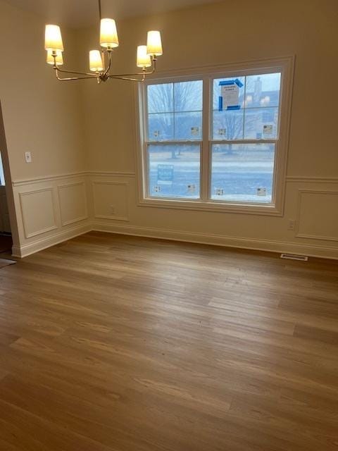 unfurnished dining area featuring wood-type flooring, a chandelier, and a wealth of natural light