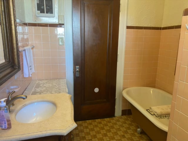 bathroom with a soaking tub, vanity, tile patterned floors, and tile walls