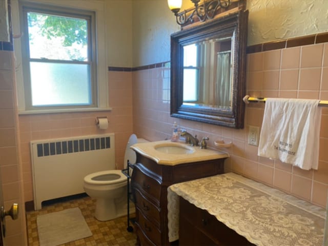 bathroom with a wealth of natural light, radiator heating unit, vanity, and tile walls
