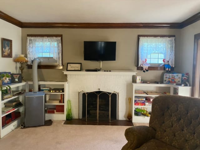 living area featuring a fireplace with flush hearth, carpet, a healthy amount of sunlight, and crown molding