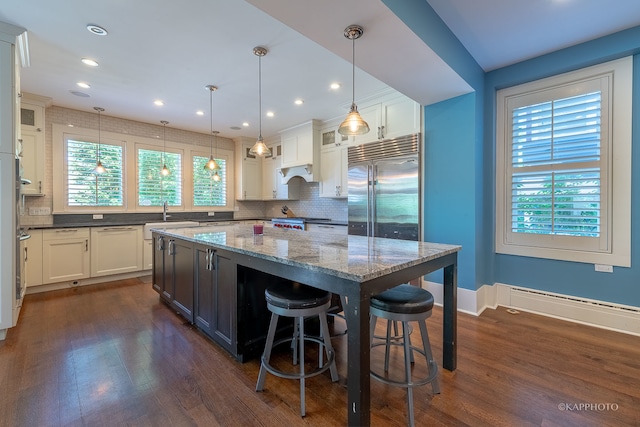 kitchen with stainless steel built in refrigerator, a center island, dark wood-type flooring, white cabinets, and decorative light fixtures