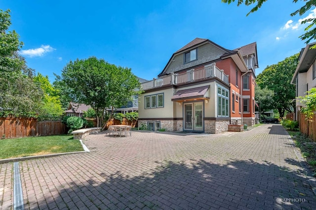 back of house featuring a balcony, a patio, french doors, and a lawn