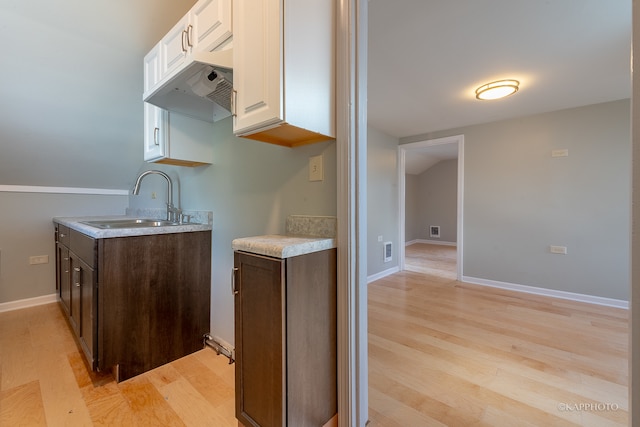 kitchen with dark brown cabinetry, light hardwood / wood-style flooring, sink, and white cabinetry