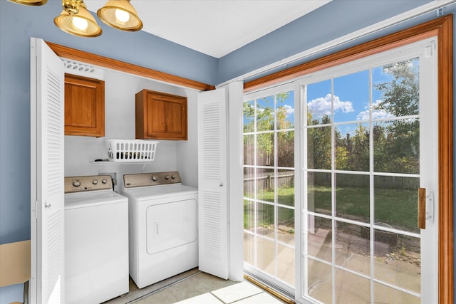 clothes washing area with light tile patterned floors, a healthy amount of sunlight, cabinets, and washing machine and clothes dryer