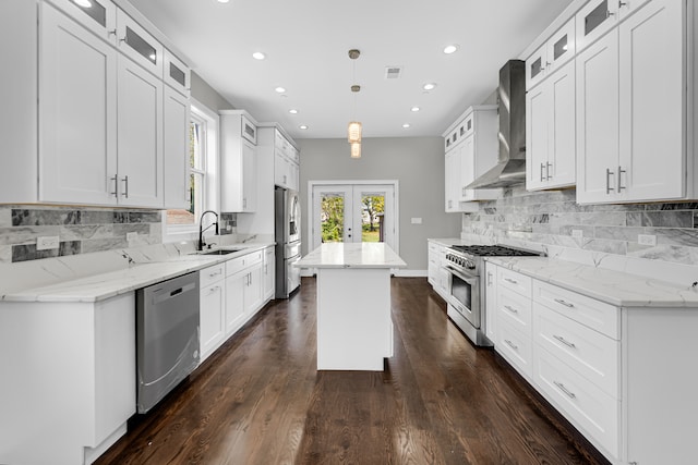 kitchen featuring stainless steel appliances, white cabinetry, wall chimney range hood, and a kitchen island