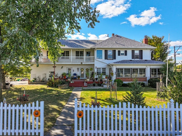 view of front of property featuring a balcony, brick siding, a fenced front yard, and a front yard