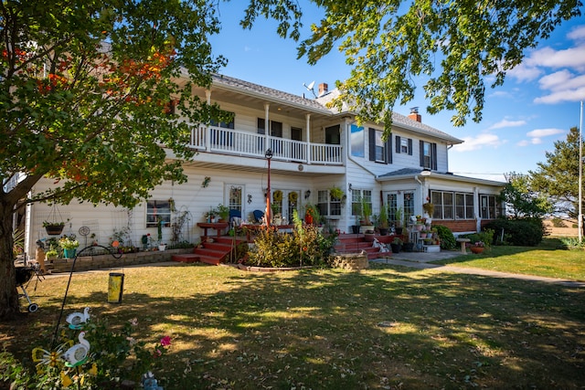 rear view of property featuring a balcony, a chimney, a lawn, and french doors