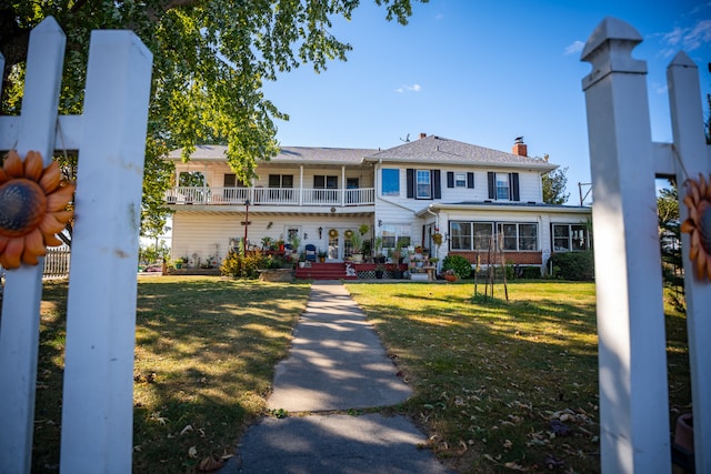 view of front of house featuring a front yard, a chimney, and a balcony