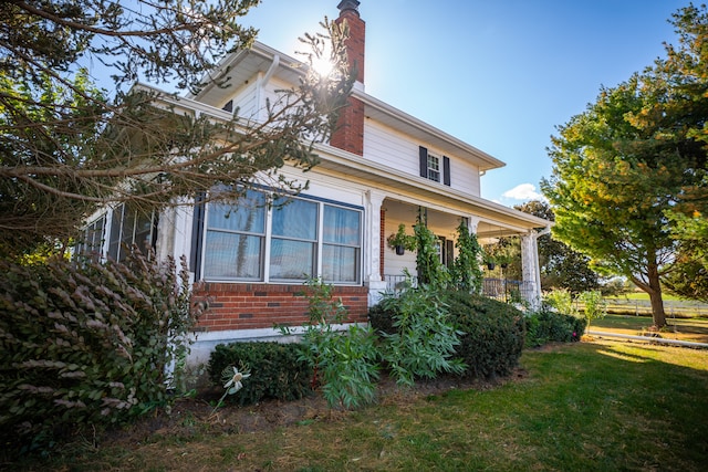 view of property exterior featuring brick siding, a chimney, a porch, and a lawn