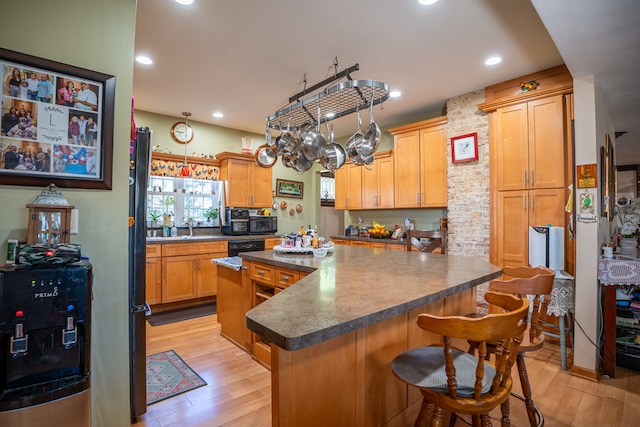 kitchen featuring a sink, a kitchen island, light wood finished floors, dark countertops, and a kitchen bar