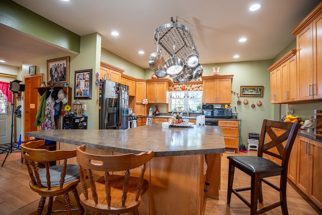 kitchen with recessed lighting, a kitchen breakfast bar, black appliances, light wood finished floors, and dark countertops